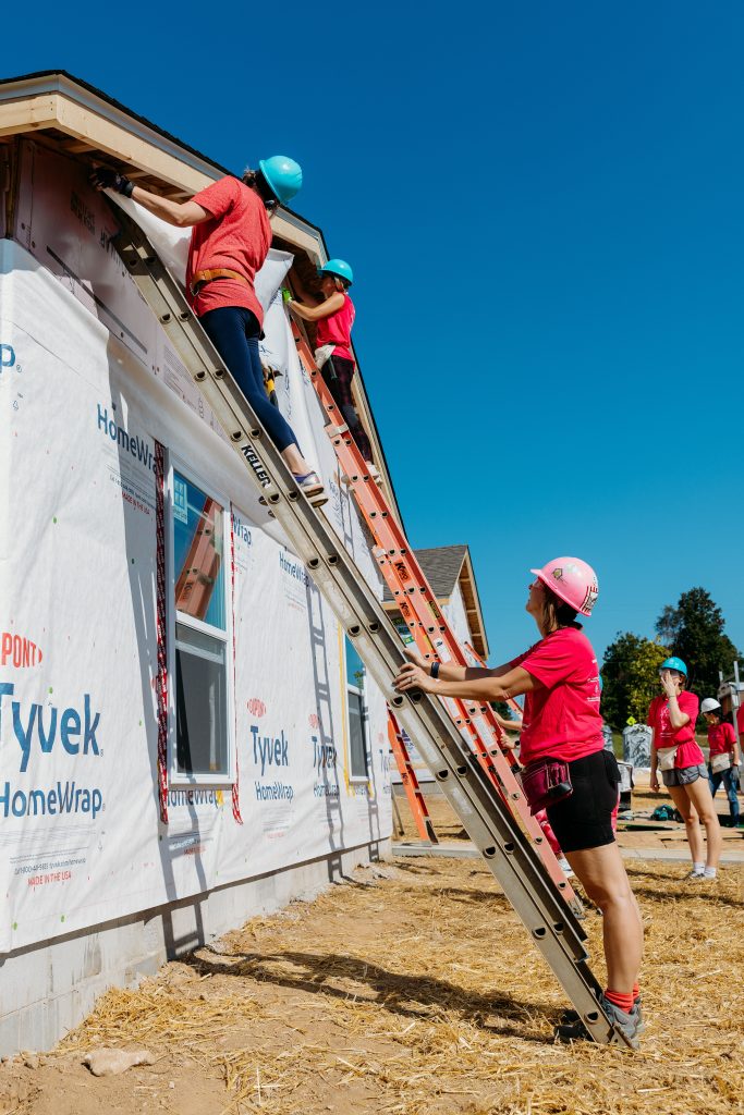 women on ladders add house wrap to a home being constructed